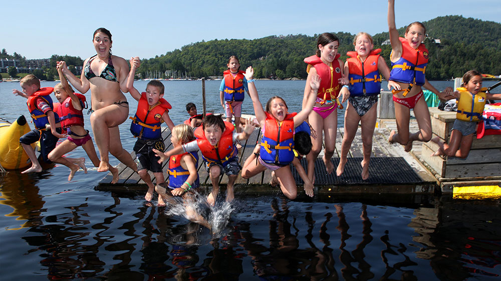 Groupe d’enfants portant des gilets de flottaison sautant dans le lac Tremblant lors du camp de jour
