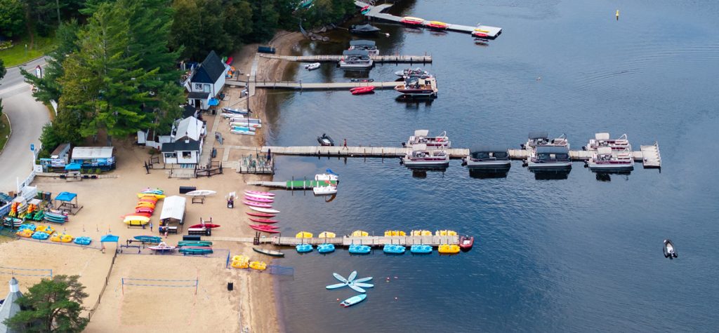 Vue aérienne de la marina de Tremblant Nautique avec plage, kayaks, pédalos, pontons et quais sur le lac.