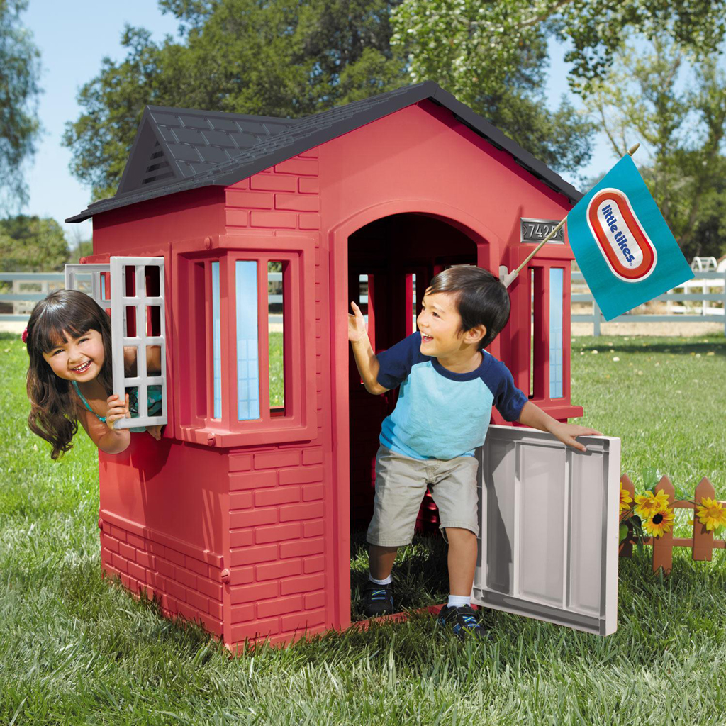 Maisonnette de jeu rouge sur un terrain gazonné, utilisée comme aire de divertissement extérieure.