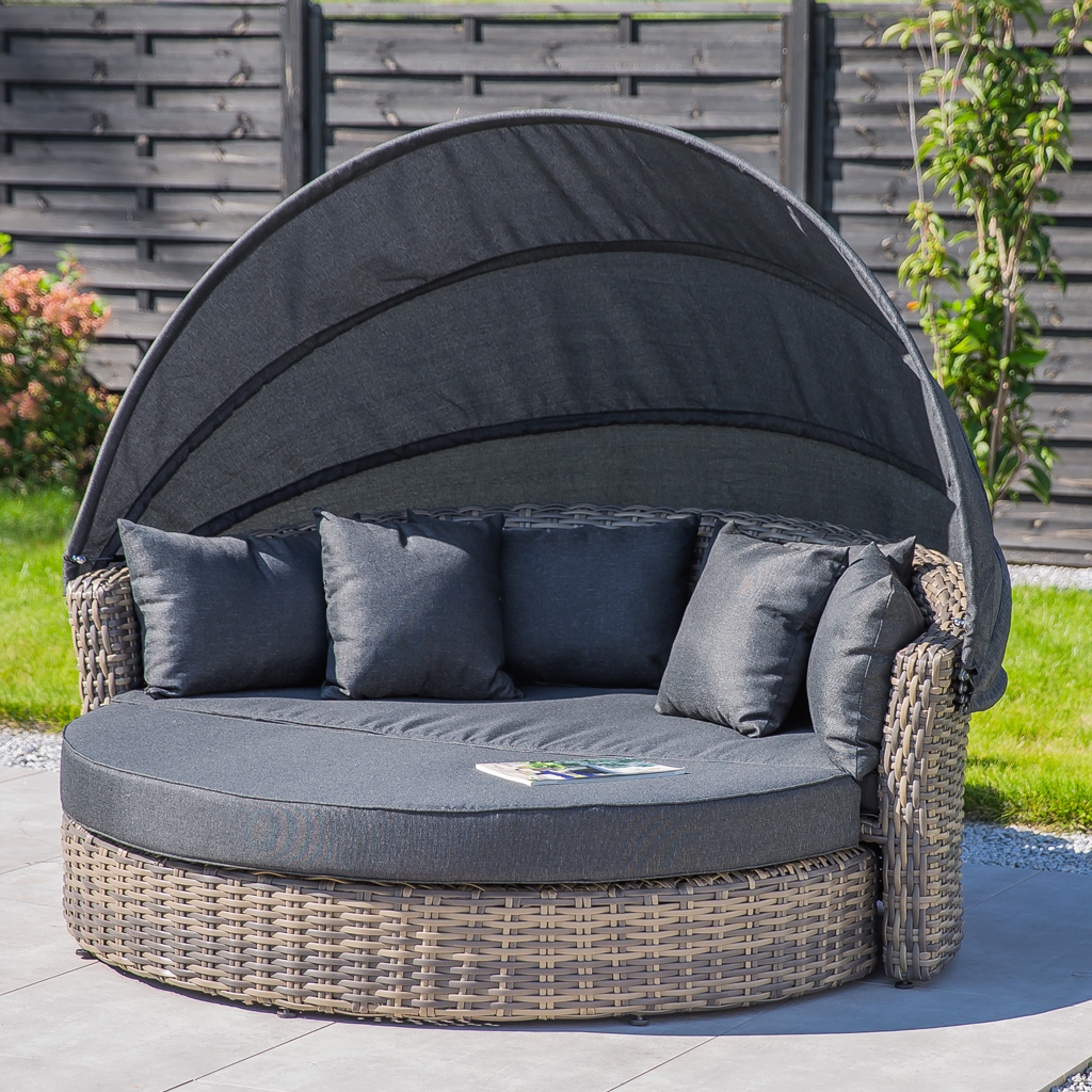 Lit de repos extérieur en rotin avec auvent rétractable et coussins gris sur une terrasse.